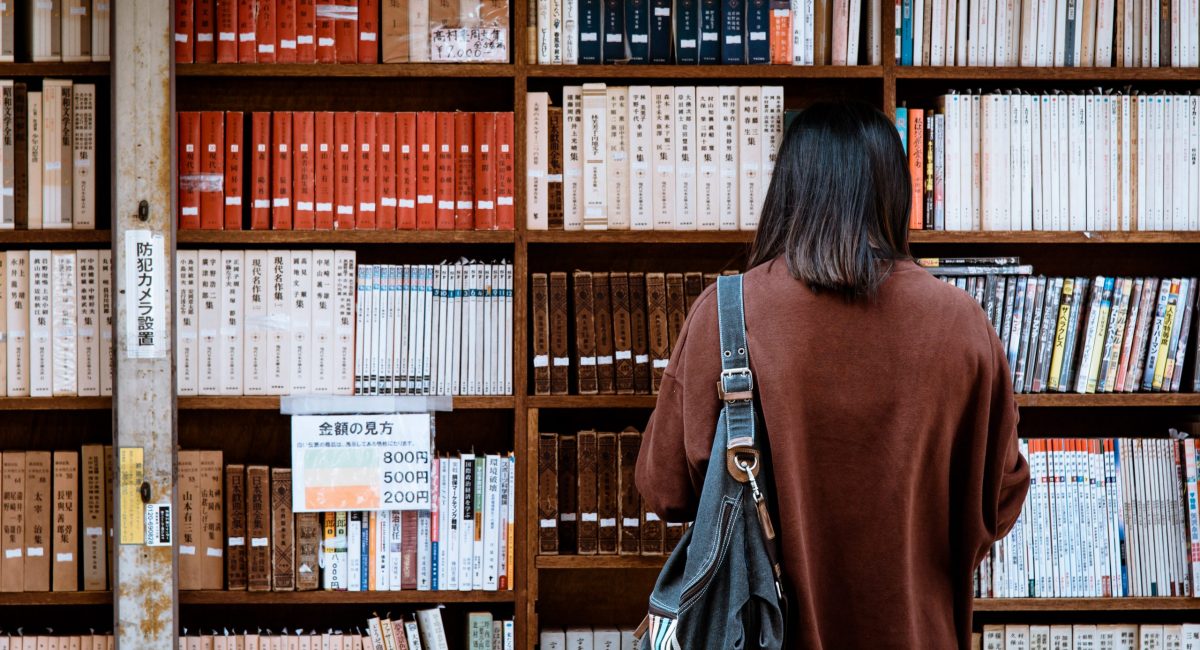 Woman wearing brown shirt carrying black leather bag on front of library books